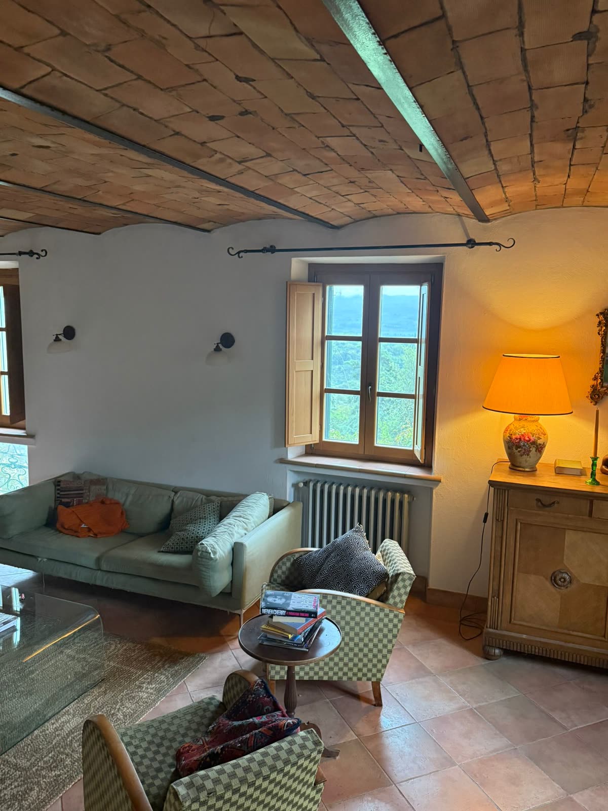 Sitting room with a vaulted brick ceiling, sofa and armchairs, and shutters open onto the countryside
