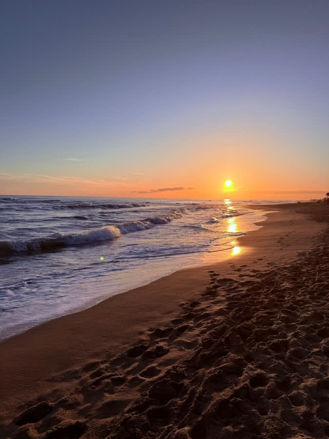 The sun setting over the sea from a wide sandy beach
