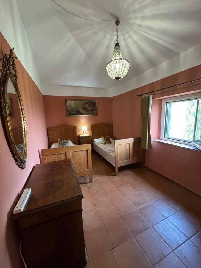 Twin bedroom with pink walls, two wooden beds and a glass chandelier