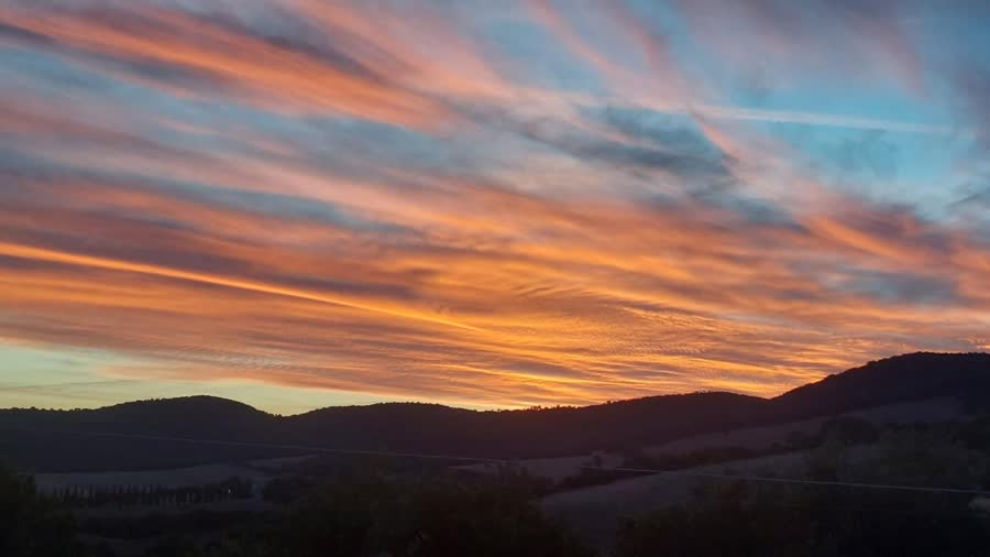 Streaked orange and blue sunset sky over dark hills