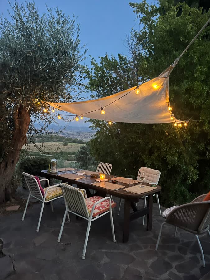 A long table laid for dinner under a canvas sail and festoon lights